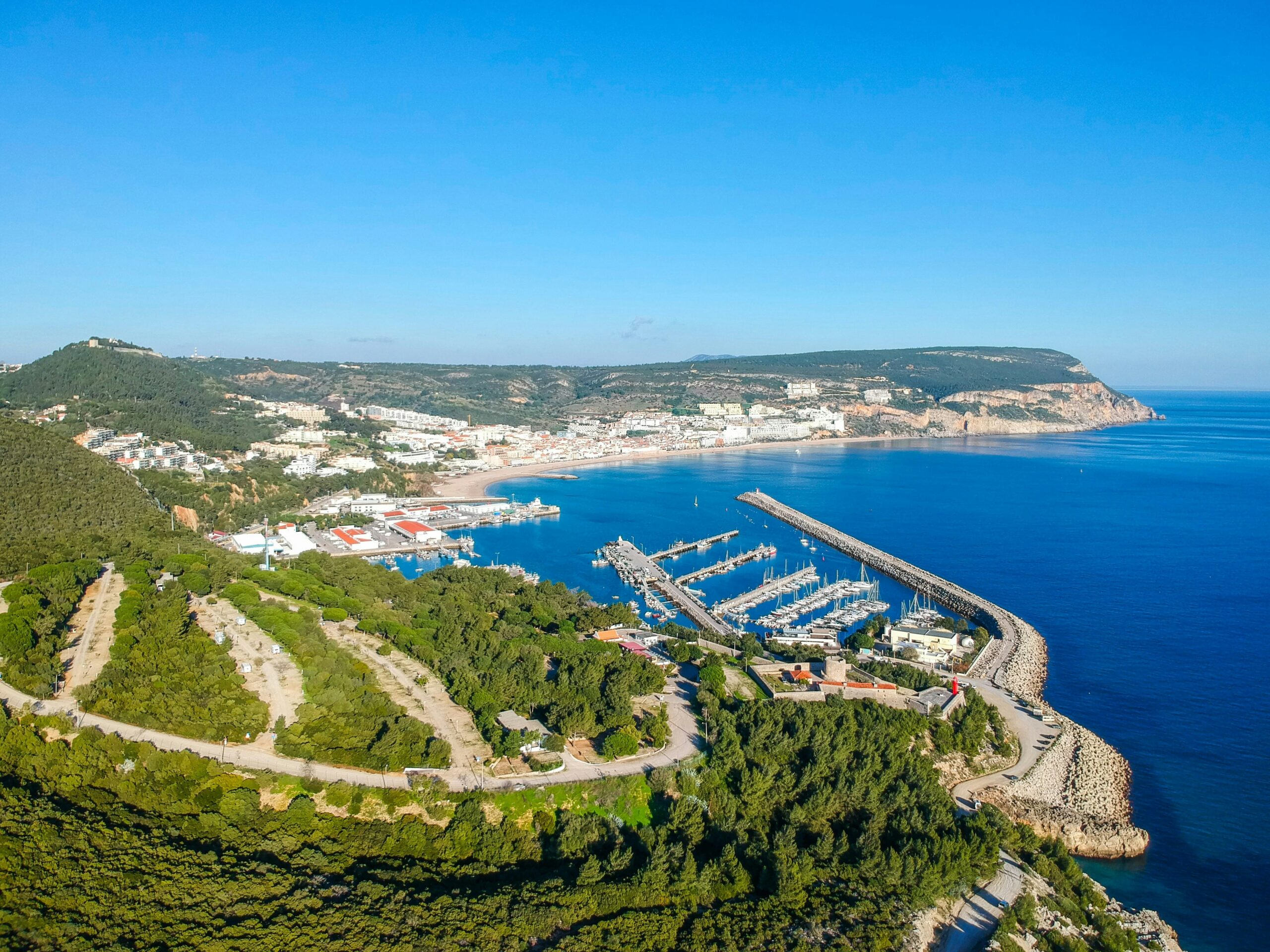 View of Setúbal, Portugal and the Sado Estuary from a higher elevation east of the city. The sun is shining, the sky is blue and the water a deep teal.